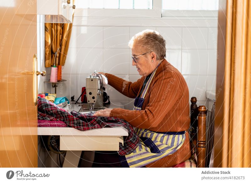 Konzentrierte ältere Schneiderin beim Nähen von Kleidung in der Werkstatt Frau Näherin nähen Stoff Faser sticken Abwasserkanal Senior Damenschneiderin