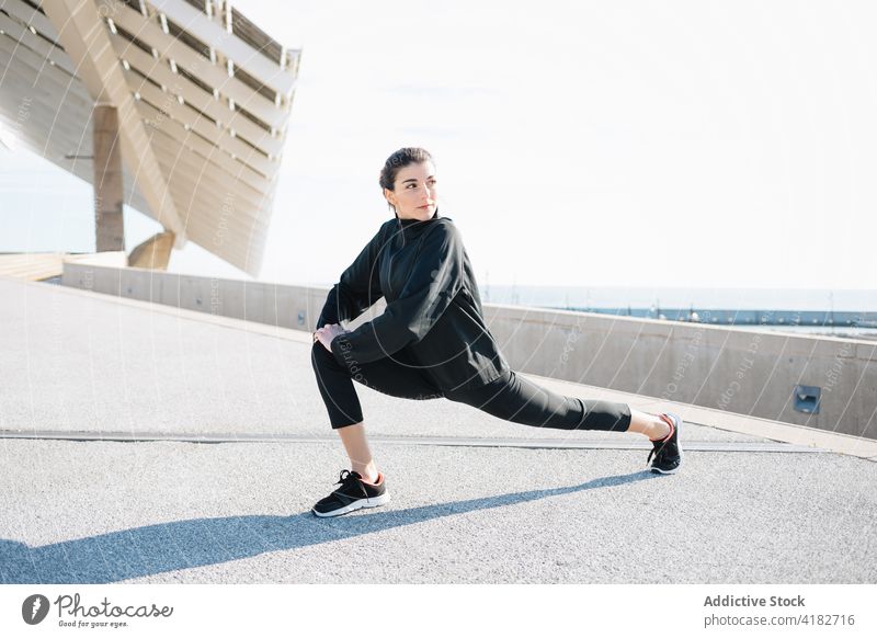 Sportliche Frau, die sich in einem Vorort die Beine vertritt Sportlerin Aufwärmen Dehnung Straße Training sportlich Vitalität schlanke physisch Fitness