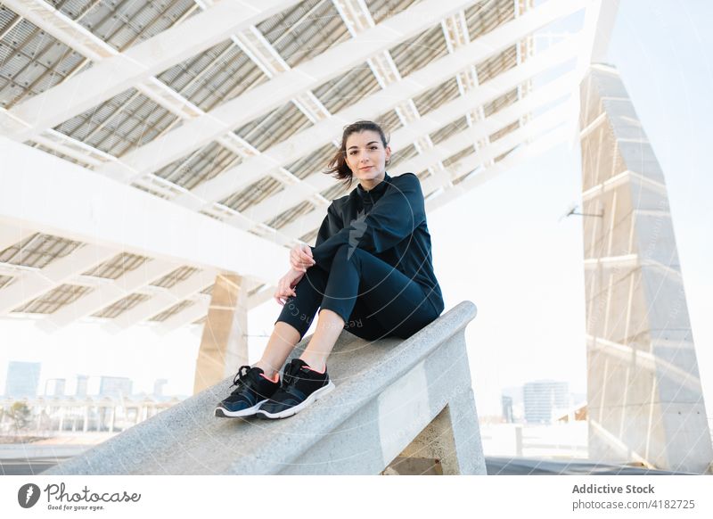 Junge Frau ruht sich auf einer Betonkonstruktion in einem Vorort aus ruhen sitzen verträumt Sportkleidung Konstruktion nachdenken Pause Vorstadt jung schlank