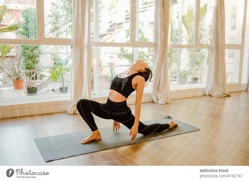 Unerkennbare Frau, die im Haus die Pose des Halbmondes auf dem Knie zeigt Yoga Gleichgewicht Halbmond-Longe auf Knie Wohlbefinden üben Energie sich zurücklehnen