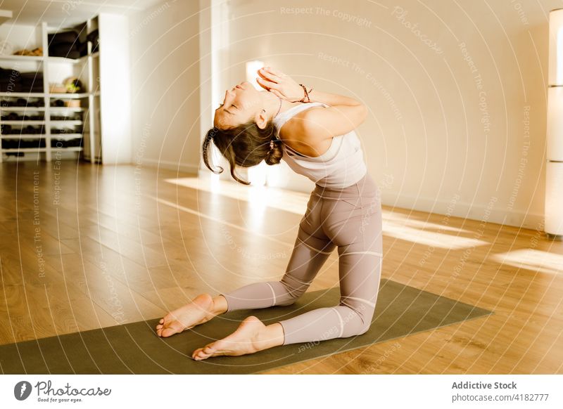 Flexible Frau in der Rückbeuge mit erhobenen Armen auf einer Yogamatte Backend Arme hochgezogen üben beweglich Dehnung Wellness Gesunder Lebensstil Haus