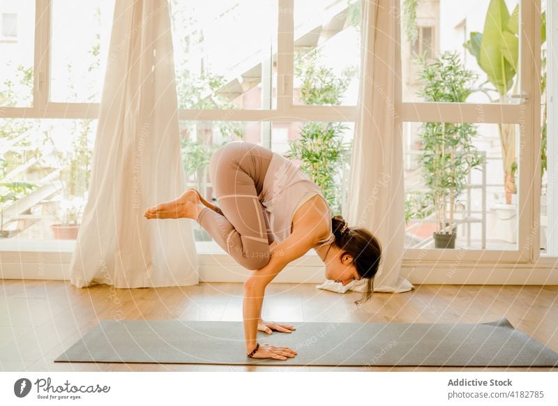 Frau zeigt Crow Pose auf Yoga-Matte im Haus Zimmer Gleichgewicht Krähenstellung Handstand Gesunder Lebensstil Talent Energie Unterlage Fenster kakasana Asana