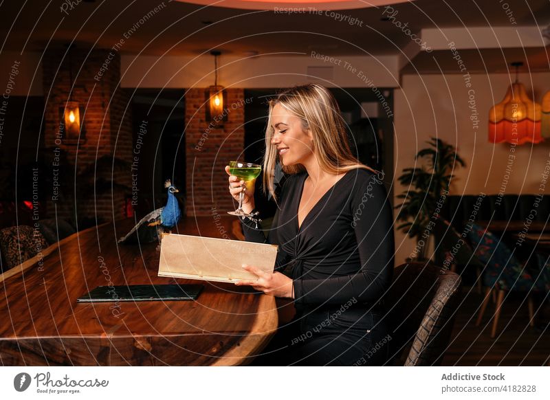 Fröhliche junge Frau trinkt einen Cocktail und liest die Speisekarte in einem schicken Restaurant trinken Bar Lächeln genießen lesen positiv Kunde Freude Stil