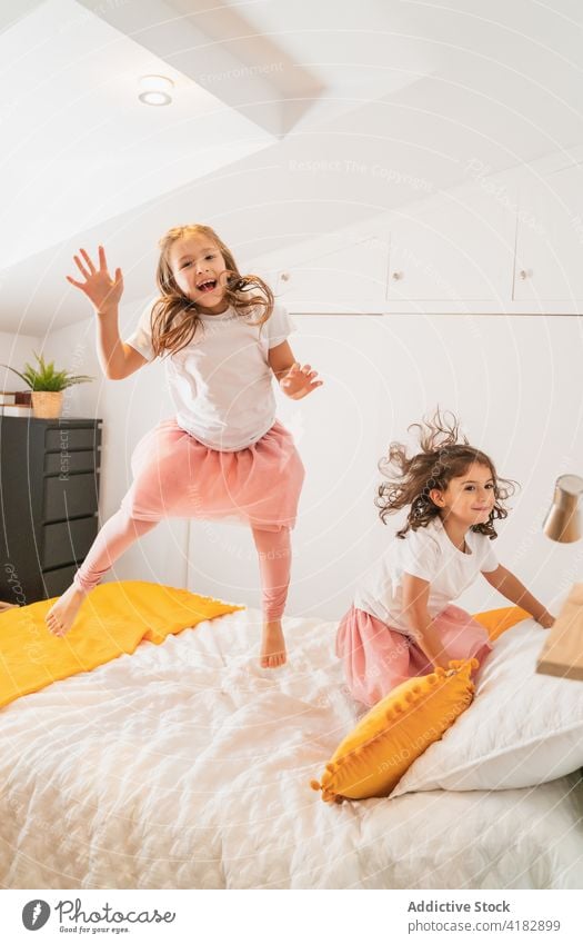 Glückliche Schwestern, die vor Aufregung auf dem Bett herumspringen Mädchen heiter Spaß haben Glee Freude Geschwisterkind Energie Kindheit lässig aufgeregt