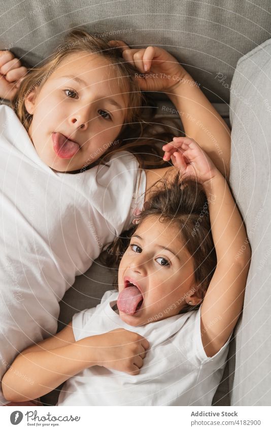 Inhalt Schwestern zeigen Zungen auf gemütlichem Sofa Mädchen ausspannen Grimasse heiter Glück Gesicht machen Zunge zeigen kindisch Spaß haben spielerisch Kinder