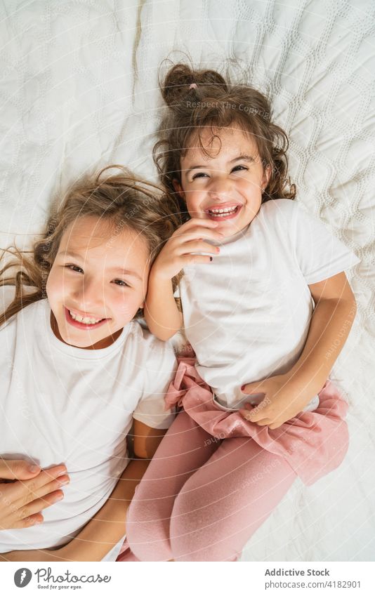 Fröhliche Schwestern liegen auf einem gemütlichen Bett und schauen in die Kamera Mädchen aufgeregt Spaß haben Freude heiter Glück Geschwisterkind Energie
