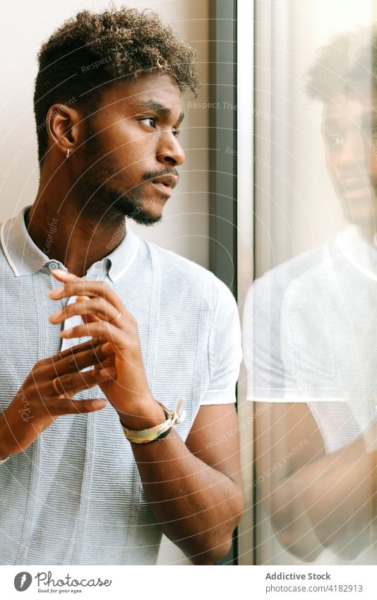 Nachdenklicher ethnischer Mann schaut zum Fenster besinnlich nachdenklich ernst Vollbart krause Haare nachdenken Denken jung schwarz Afroamerikaner männlich