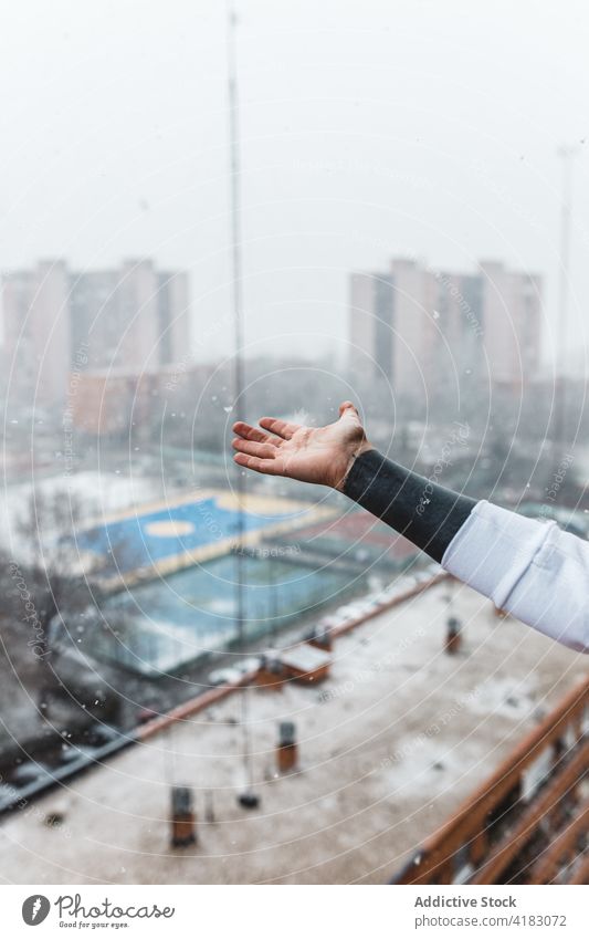 Gesichtslose Person, die auf dem Balkon Schneeflocken mit der Hand auffängt fangen Schneefall Winter Großstadt Wetter Saison urban cool Freude Frost kalt Straße