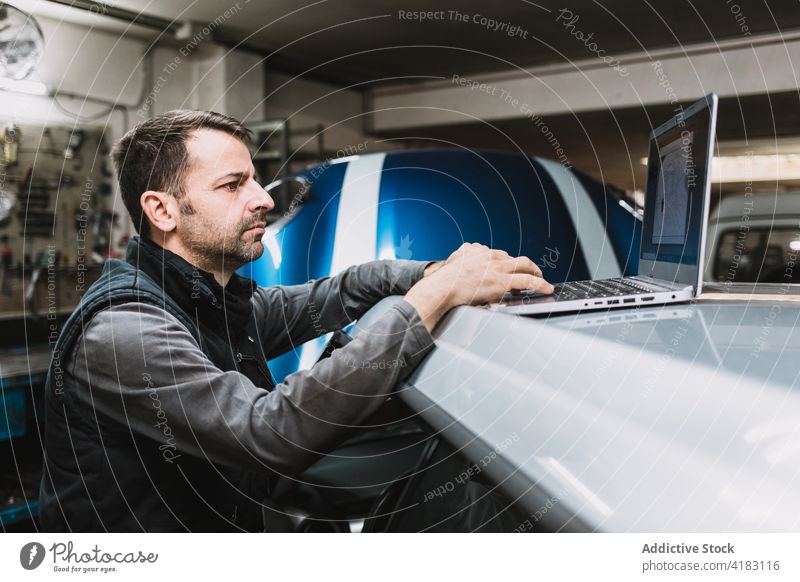 Aufmerksamer männlicher Mechaniker, der in der Werkstatt auf einem Laptop tippt Tippen Bildschirm achtsam Internet Mann Auto benutzend Apparatur Gerät Netbook