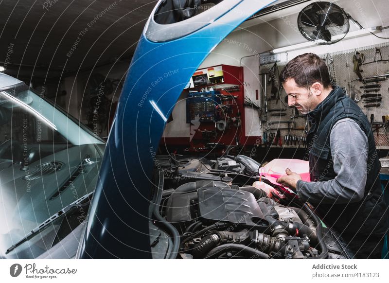 Lächelnder Mechaniker, der in einer Autowerkstatt Kühlmittel in den Kühler gießt eingießen Heizkörper Kapuze Fahrzeug Flugzeugwartung Mann Arbeit Garage