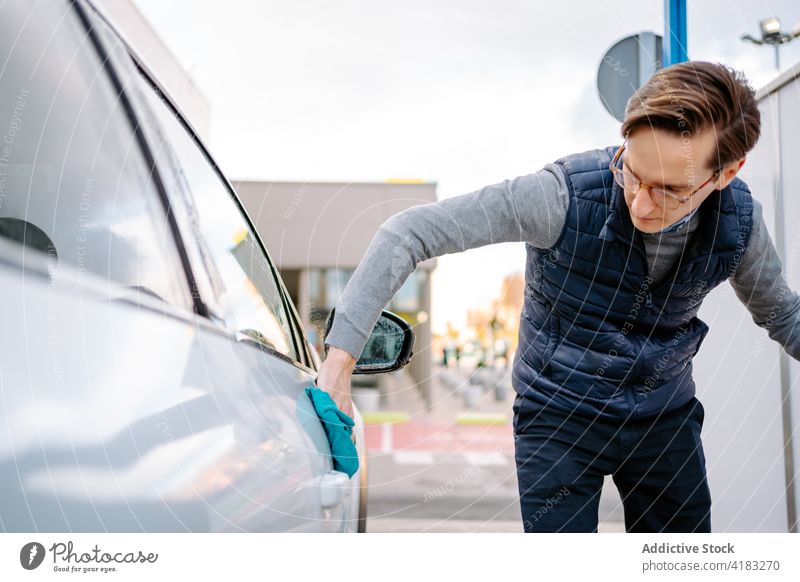 Konzentrierter junger Mann, der sein Auto mit einer Serviette abwischt PKW Waschen Wischen Tuch Fokus Fahrzeug Selbstbedienung Station Straße Fenster Wasser