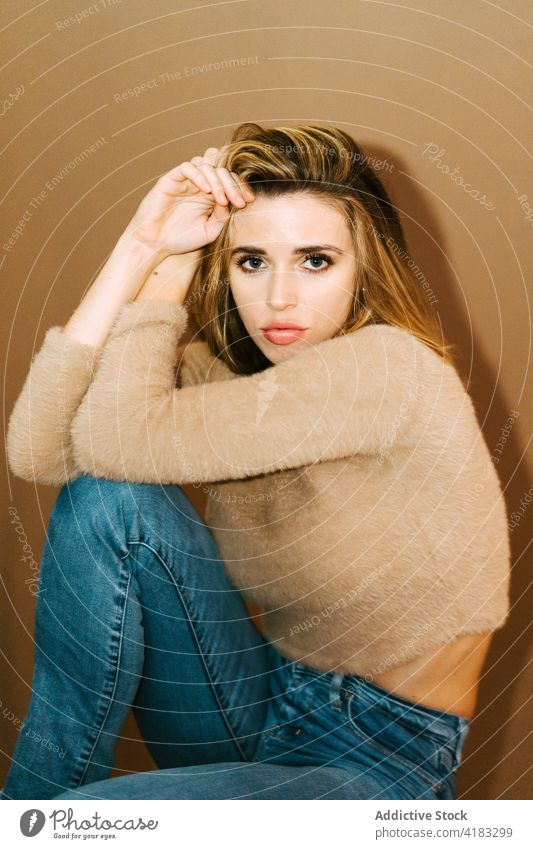 Stilvolle Frau im Atelier sitzend trendy Pullover jung Model Haare berühren selbstbewusst Jeanshose lässig Outfit Vorschein Kleidung Bekleidung Kleidungsstück