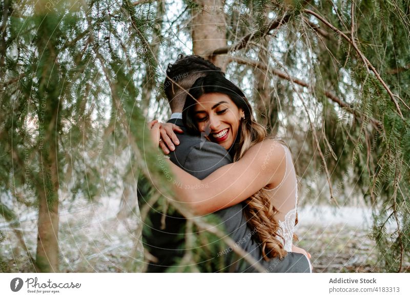 Fröhliches junges ethnisches Paar umarmt sich im Wald am Hochzeitstag Umarmung Lächeln Zusammensein Liebe Partnerschaft romantisch Zuneigung Heirat nadelhaltig