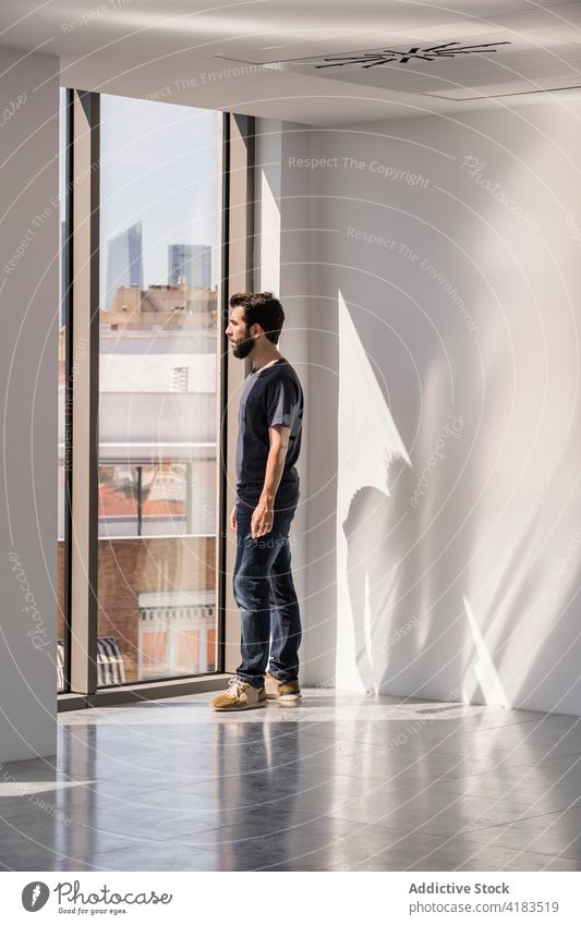 Mann steht am Fenster in einer geräumigen Bürohalle leer Saal Einrichtung Schatten Sonnenlicht Geometrie männlich Innenbereich Form Flur weiß Wand modern Design