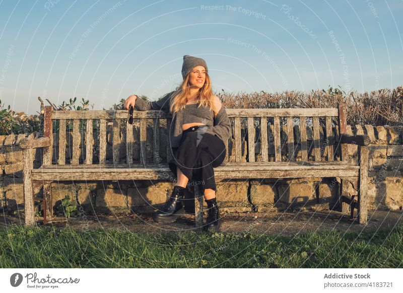 Glückliche Frau in warmer Strickkleidung auf einer Bank ruhend Natur Herbst heiter Reisender genießen sonnig jung reisen Lifestyle sich[Akk] entspannen Stil
