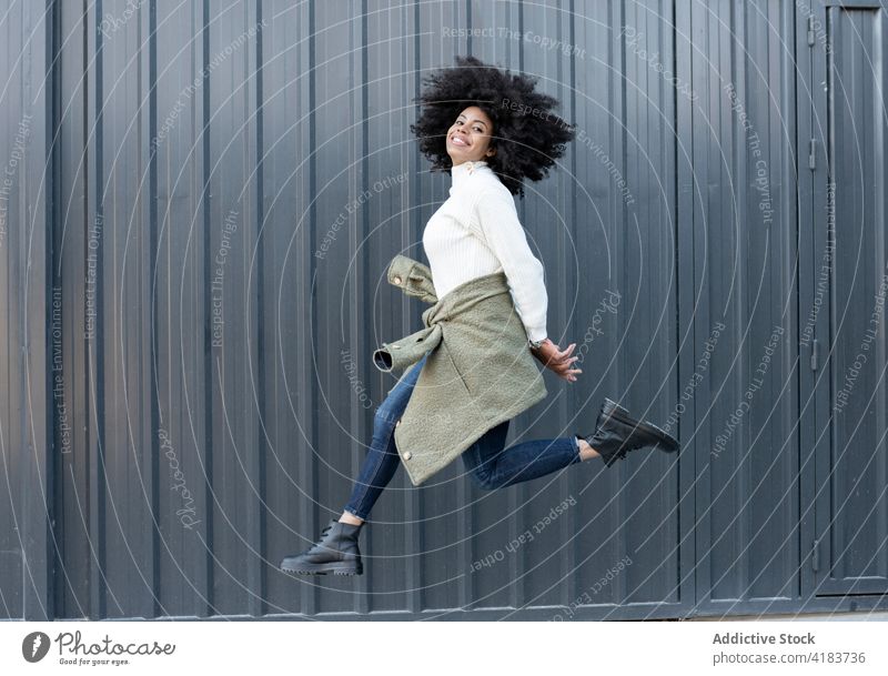 Selbstbewusstes junges schwarzes Mädchen springt auf die Straße Frau springen Lächeln trendy positiv Freude Bewegung aufgeregt Inhalt Energie expressiv
