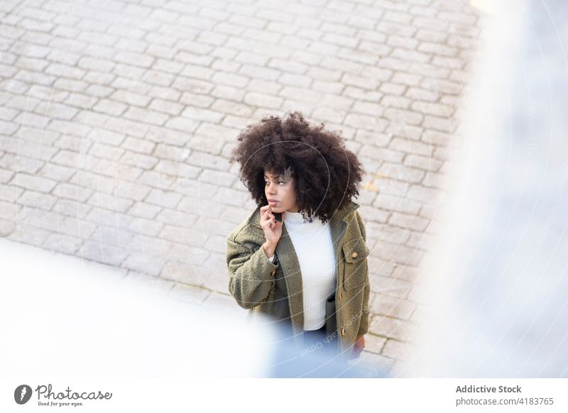 Seriöse junge schwarze Frau, die auf der Straße geht und mit ihrem Smartphone spricht Telefonanruf Spaziergang Konzentration Stil Gespräch Kommunizieren