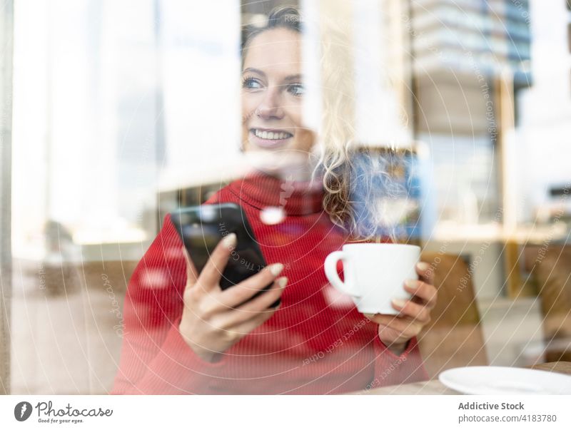 Lächelnde Frau mit Smartphone und Tasse in einem Cafe Café genießen heiter trinken Browsen Getränk sorgenfrei Internet heiß Tisch sitzen Heißgetränk Mobile