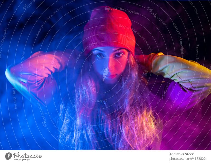 Junge weibliche Millennials stehen mit den Händen hinter dem Kopf in einem verrauchten Neonraum Frau Stil neonfarbig Rauch selbstbewusst Vorschein Porträt Mode