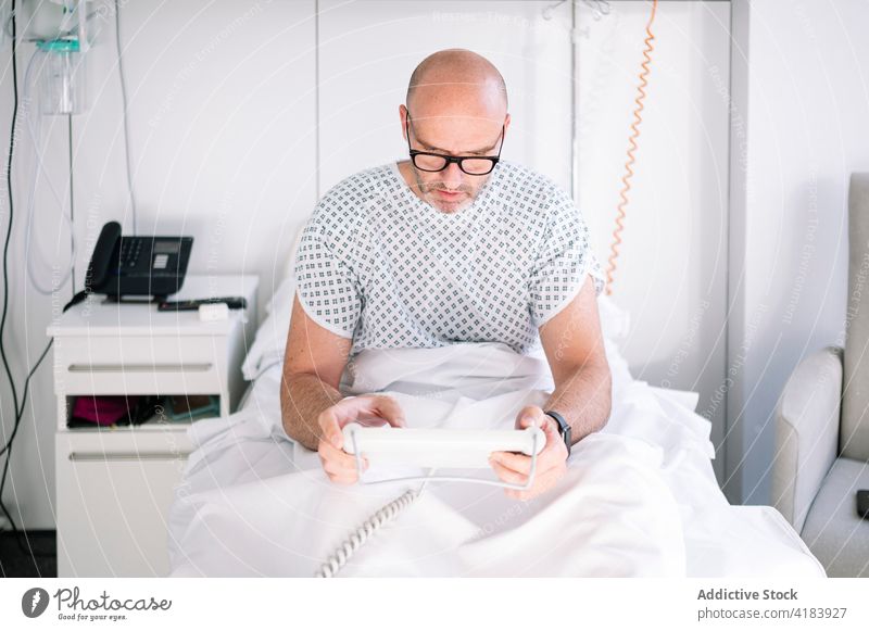 Fokussierter männlicher Patient mit Tablette auf dem Stationsbett Mann geduldig Bett benutzend Arbeitstier Gerät Krankenhaus Klinik zuschauen professionell