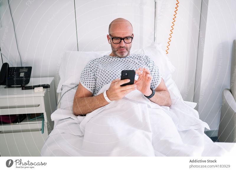 Fokussierter männlicher Patient beim Telefonieren auf dem Stationsbett Mann geduldig Bett Smartphone benutzend Mobile Arbeitstier Gerät Krankenhaus Klinik