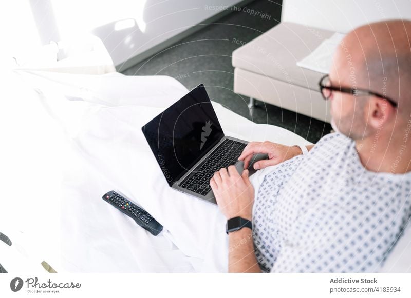 Schwerer männlicher Patient arbeitet am Laptop auf dem Stationsbett Mann geduldig Bett Arbeit ernst Fokus Arbeitstier Krankenhaus Gerät Klinik zuschauen