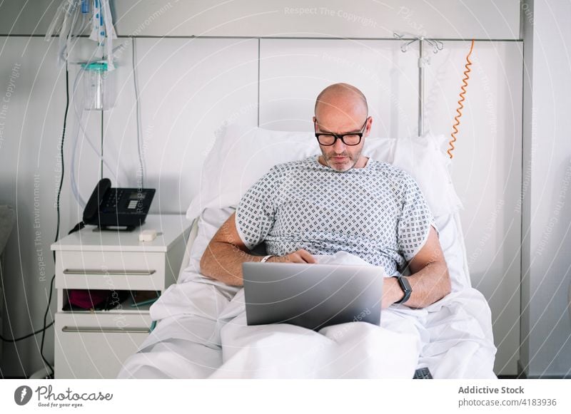 Schwerer männlicher Patient arbeitet am Laptop auf dem Stationsbett Mann geduldig Bett Arbeit ernst Fokus Arbeitstier Krankenhaus Gerät Klinik zuschauen