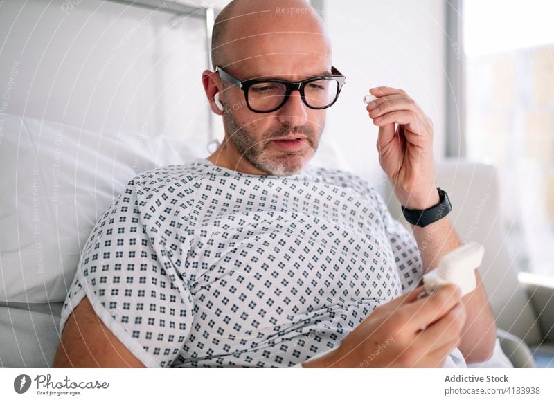 Ein männlicher Patient, der sich auf der Station Ohrstöpsel aufsetzt Mann geduldig tws Bett Krankenhaus zuhören Gesundheitswesen Medizin Gerät Klinik zuschauen