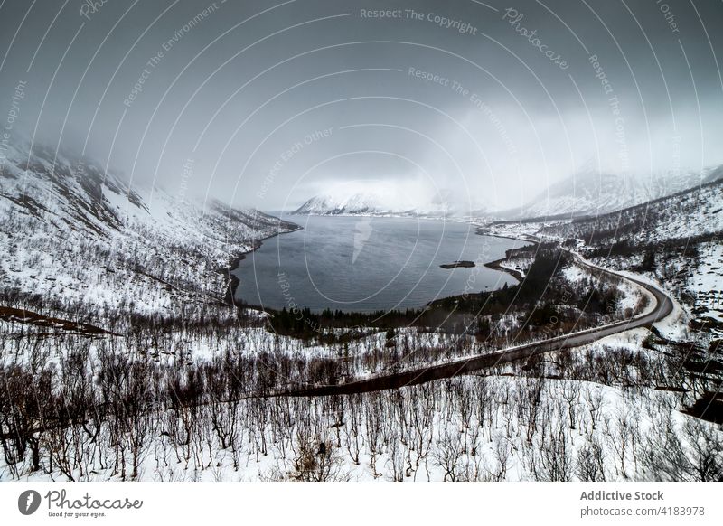 Straße in verschneiten Bergen in der Nähe eines Sees im Winter Berge u. Gebirge Schnee Landschaft endlos Fahrbahn majestätisch Norwegen wolkig Himmel kalt