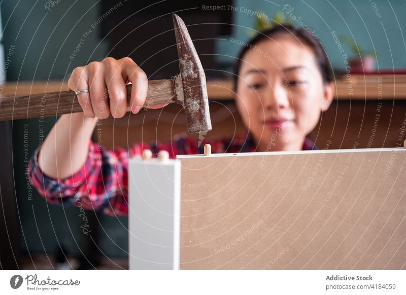 Asiatische Frau beim Zusammenbau von Möbeln zu Hause versammeln Hammer Dübel nageln hölzern neu heimwärts Fokus ethnisch asiatisch wohnbedingt ernst