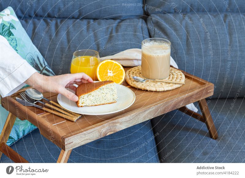 Crop-Frau mit Frühstück auf dem Tablett zu Hause Kuchen Biskuit Dessert Kaffee Saft Morgen heimwärts Spielfigur nehmen Scheibe Tasse selbstgemacht Schwamm