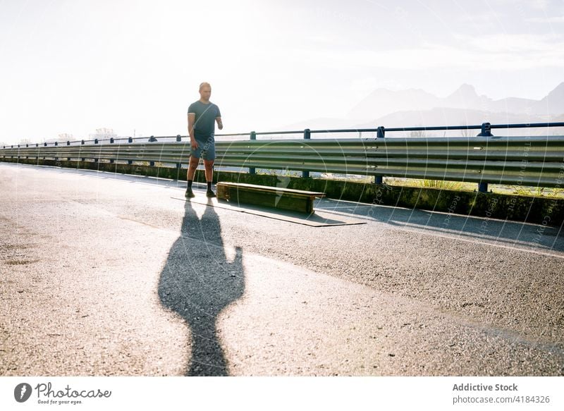 Behinderter Sportler trainiert auf einer Brücke im Sonnenlicht vorbereiten Übung Training Bank Himmel Schatten Mann Landschaft rau Straße Zaun hell glänzend
