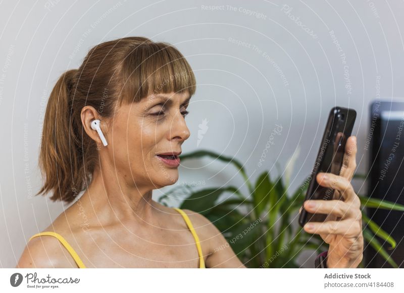 Positive erwachsene Frau mit Videoanruf über Smartphone heiter Video-Chat Wohnzimmer Ohrstöpsel reden diskutieren Erwachsener abgelegen positiv Talkrunde
