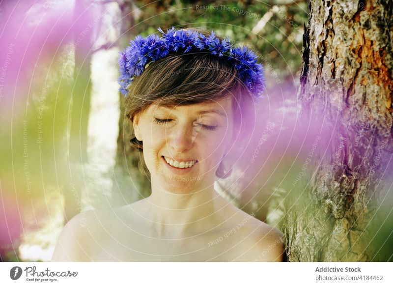 Romantische Frau mit Kranz auf dem Kopf, die sich im Park im Sonnenlicht ausruht ruhen Wald friedlich Windstille romantisch Natur Harmonie Stil Baum Kofferraum