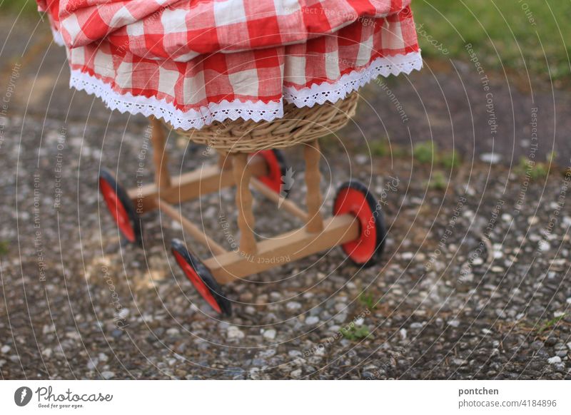 vintage Puppenwagen aus Korb und Holz puppenwagen rot-weiß korb holz stoff kinderspielzeug kinderwagen rollen beton draußen Kindheit