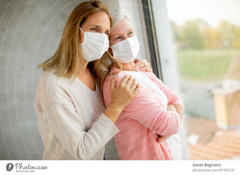 Ältere Frau mit pflegender Tochter zu Hause mit medizinischen Masken Erwachsener Pflege Kaukasier Korona Coronavirus Krankheit Holunderbusch älter Seuche