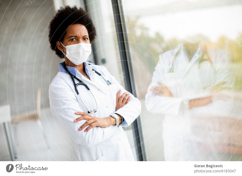 Schwarze Ärztin stehend am Bürofenster mit Gesichtsschutzmaske Erwachsener schwarz Klinik Kontemplation unzufrieden Arzt Seuche Kompetenz Frauen Krankenhaus