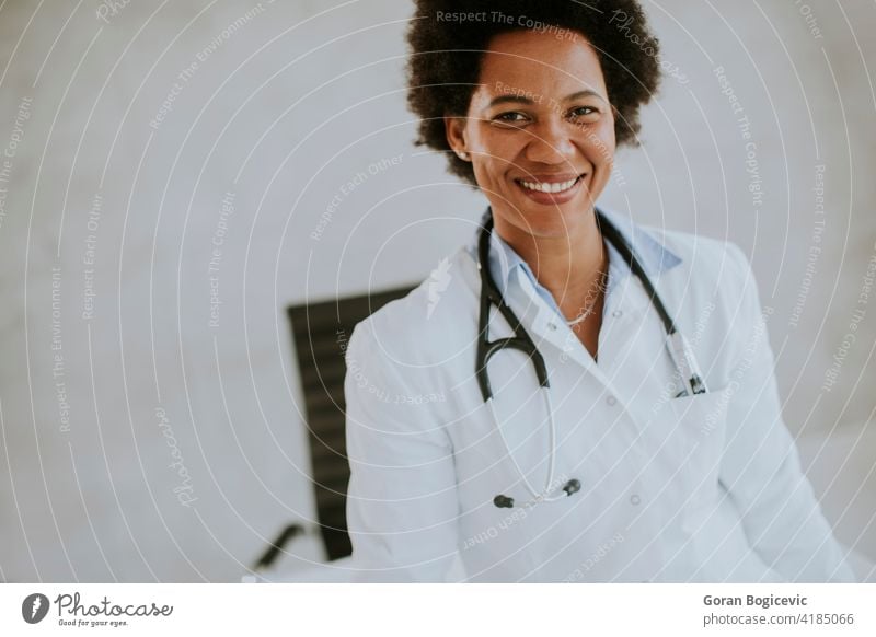 Weiblicher afroamerikanischer Arzt in weißem Kittel mit Stethoskop steht am Schreibtisch im Büro Erwachsener Afrikanisch Amerikaner schön schwarz Klinik