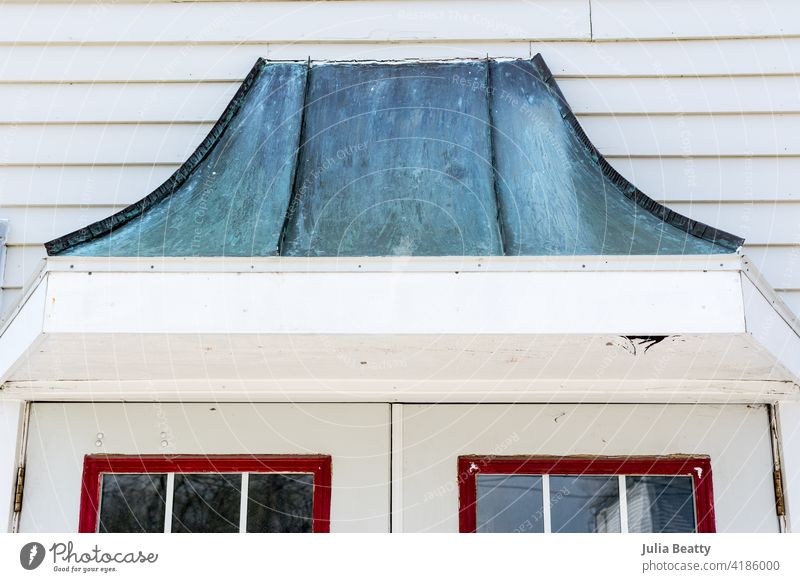 Metallgiebel mit türkisfarbener Patina über einer Reihe von Fenstertüren mit roter Zierleiste; alte Fassade eines Kleinstadtgebäudes Dachgiebel Dachgaube