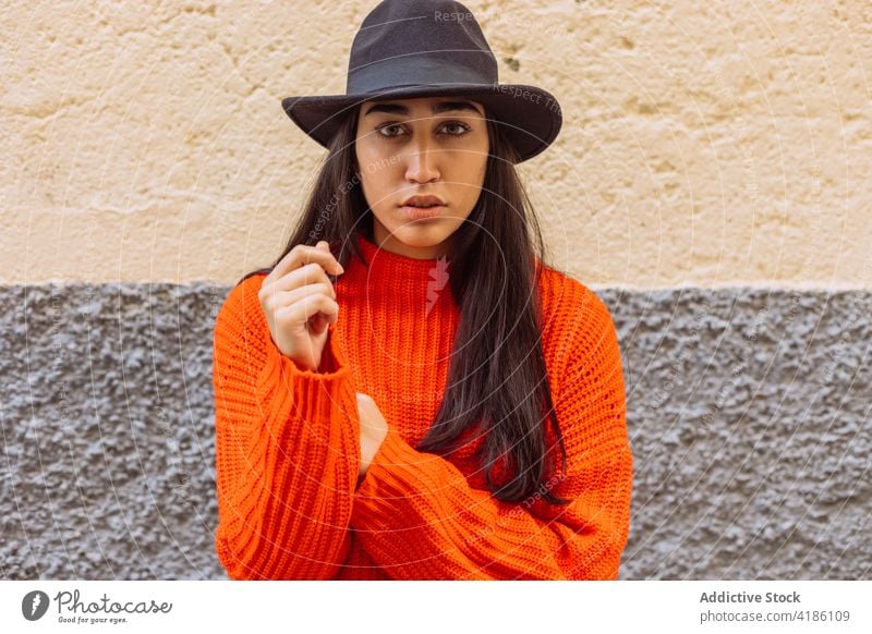 Stilvolle Frau mit Hut steht in der Nähe von Backsteinmauer Mode Strickwaren trendy Farbe hell orange jung ethnisch gestrickt Lifestyle Backsteinwand