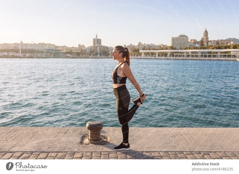 Schlanke Sportlerin, die ihre Beine an einer Böschung ausstreckt Frau Training Übung Dehnung Stauanlage Fitness passen Aufwärmen Hafengebiet Wellness Gesundheit