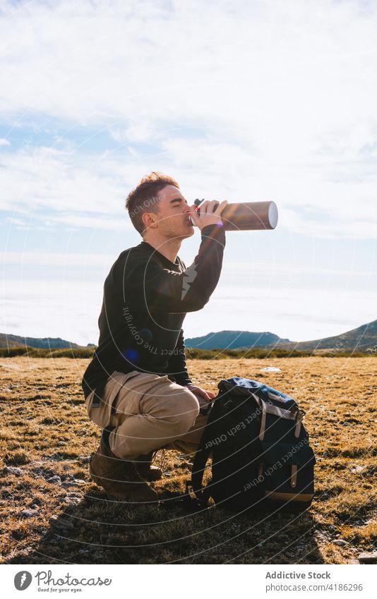 Junger männlicher Wanderer, der ein heißes Getränk genießt, während er am Berghang sitzt Mann trinken Thermoskanne Reisender Wanderung Ausflug