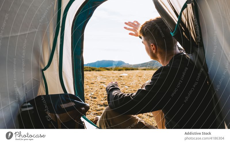 Junger nachdenklicher Camper entspannt sich im Zelt am sonnigen Morgen Mann ruhen Lager verträumt Reisender Berge u. Gebirge bewundern Ausflug