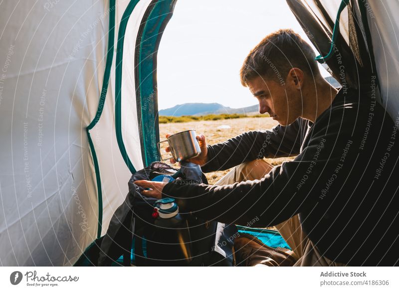 Junger Mann trinkt heißes Getränk im Campingzelt Heißgetränk Zelt Lager Wanderung reisen ruhen Windstille Wohnmobil Natur Berge u. Gebirge Hügel Trekking