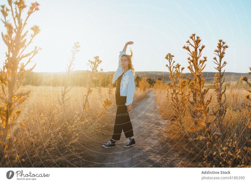 Stilvolle junge Frau tanzt auf dem Lande im Sonnenlicht Tanzen Feld Landschaft Natur sich[Akk] bewegen selbstbewusst aktiv Feiertag Pflanze trendy trocknen Gras