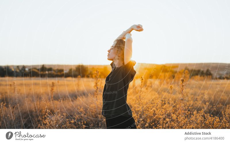 Entspannte junge Frau mit erhobenen Armen im Feld Arme hochgezogen genießen Landschaft Sonnenuntergang sich[Akk] entspannen Natur Anmut ruhen idyllisch lässig