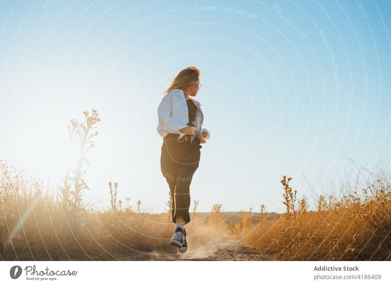 Friedliche junge stilvolle Dame, die während der Ferien auf dem Lande auf einem Pfad in einem Feld läuft Frau laufen Landschaft Straße ländlich Natur Hügelseite