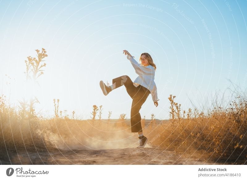 Stilvolle junge Frau tanzt auf dem Lande im Sonnenlicht Tanzen Feld Landschaft Natur sich[Akk] bewegen selbstbewusst aktiv Feiertag Pflanze trendy trocknen Gras