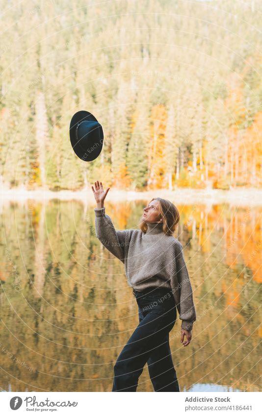 Frau wirft Hut in die Luft, während sie gegen einen See läuft werfen Spaziergang Baum Reflexion & Spiegelung Natur achtsam Reisender lässig Stil Ausflug Outfit