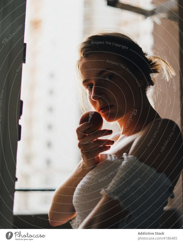 Schöne Frau mit Pfirsich stehend in moderner Küche verträumt Snack Gelassenheit positiv friedlich feminin Abfertigungsschalter ruhig charmant nackte Schultern